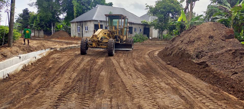 Yellow road grader leveling a dirt road beside new drainage